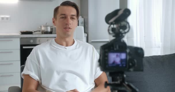 Millennial blogger nebo vlogger muž natáčení nového vlog videa s profesionální kamerou, namontované na stativ sedí na pohovce doma. - Záběry, video