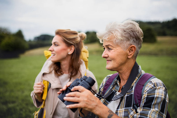 Happy senior mother hiker with adult daughter holding binoculars outdoors in nature - Foto, immagini