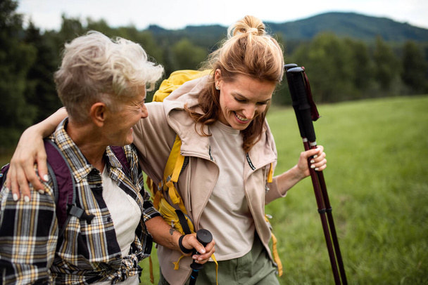 Happy mid adult woman with trekking poles hiking with active senior mother outdoors in nature. - Foto, Bild