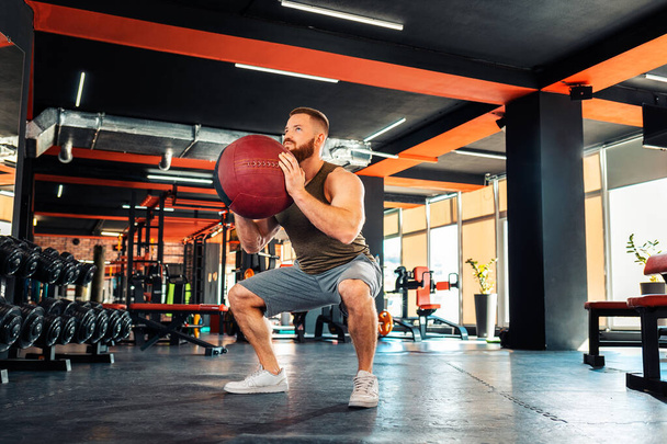Young bearded athletic man training in the gym with a medicine ball. The concept of fitness and work out. - Фото, зображення