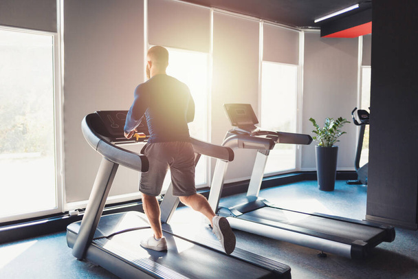 A sporty man runs on a treadmill in the gym. Keeping fit with cross training. Back view. - Φωτογραφία, εικόνα