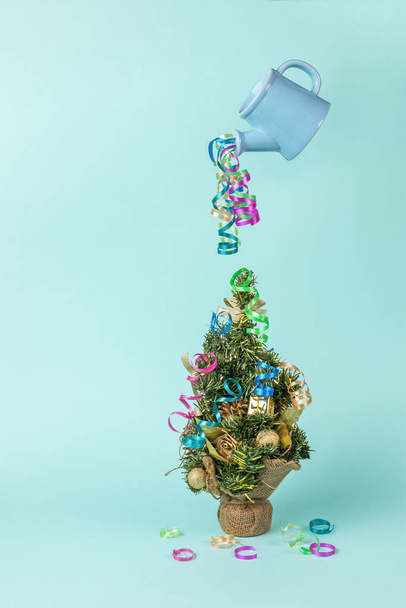 Eine bunte Luftschlange, die aus einer schwimmenden Gießkanne auf einen Weihnachtsbaum strömt. Das Minimalkonzept für das neue Jahr. Zeitgenössische Kunst. Platz für Text. - Foto, Bild