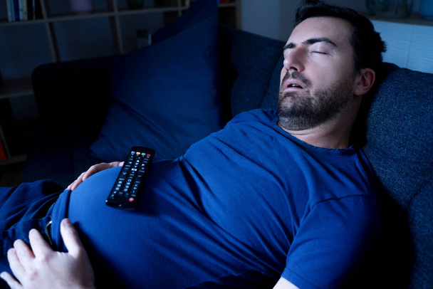 Один парень спит на диване ночью и смотрит телевизор. - Фото, изображение