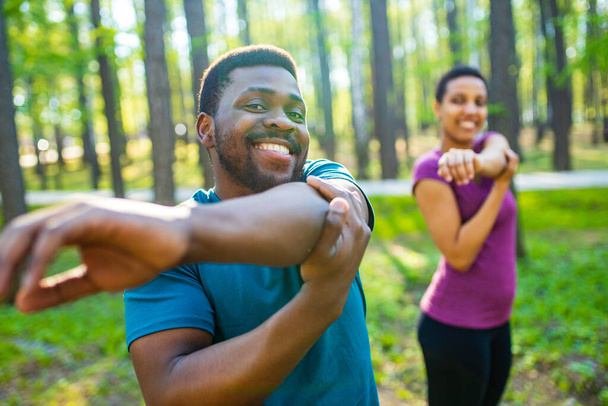 Young man and beautiful woman doing stretching exercises outdoors - Photo, Image