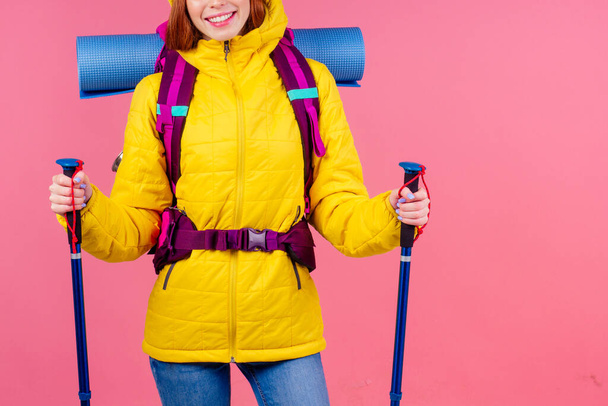 caucasian redhaired ginger woman with backpack and karemat in studio pink background. Ready for mountain adventure nordic walking - Photo, image