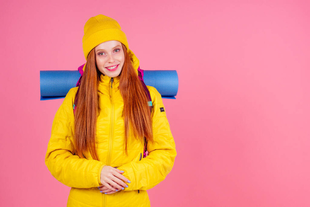 caucasian redhaired ginger woman with backpack and karemat in studio pink background. Ready for mountain adventure - Photo, Image