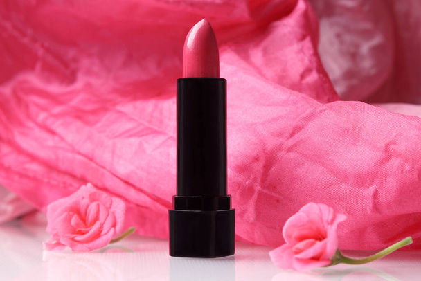Lápiz labial rosa en un tubo negro con flores de pelargonio frescas. Cosmética decorativa. - Foto, imagen