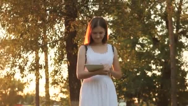 Egy lány tanul egy táblagépen a város napsugaraiban, napnyugtakor online vásárol egy online boltban, megnézi a leveleket a közösségi oldalakon, csevegnek, könyveket olvas és híreket az oldalak információs forrásaiban - Felvétel, videó