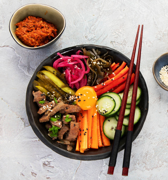 Bibimbap con snacks sobre fondo gris. Comida tradicional coreana. Vista superior, plano, espacio para copiar - Foto, Imagen