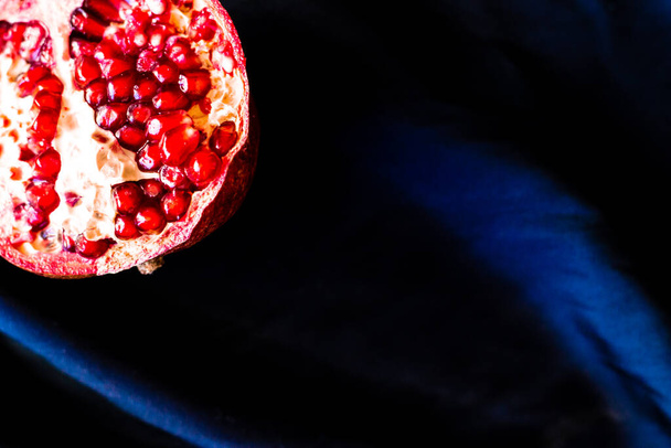 Close up foto van gesneden rijpe rode granaatappel op donkerblauwe stof achtergrond - Foto, afbeelding