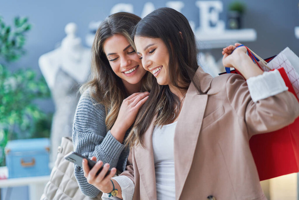 Zwei glückliche schöne Mädchen, die beim Einkaufen ihr Handy in der Hand halten - Foto, Bild