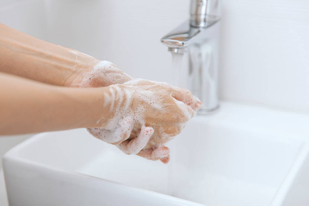 Washing hands under the flowing water tap. Hygiene concept hand detail. Washing hands rubbing with soap for corona virus prevention, hygiene to stop spreading corona virus in or public wash room - Φωτογραφία, εικόνα