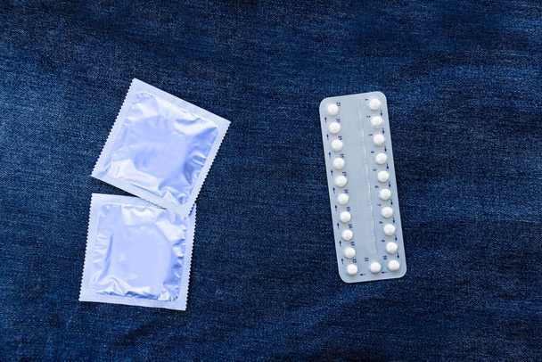 contraceptive pills and condoms on denim background. Family planning. Selective focus. Copy space.Pregnancy planning. Sexuality education for adolescents. Contraceptives for women and mann. Prevent HIV disease. - Photo, Image