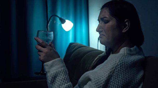 Depressed woman drinks alcohol at darkness of living room - Photo, Image