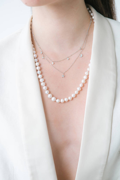 Trending silver necklace with pearls on a beautiful young girl in a white fashionable jacket. Beauty and fashion  - 写真・画像