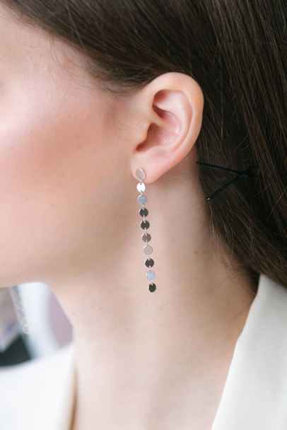 Trendy silver earrings  on a beautiful young girl with long dark hair. Beauty and fashion  - 写真・画像