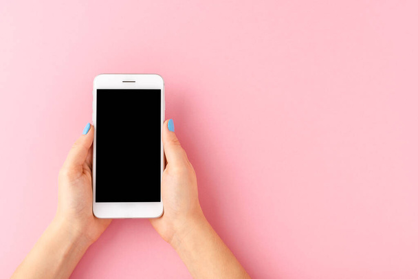 Female hands holding smart phone with empty screen on pink background. Top view - Photo, Image