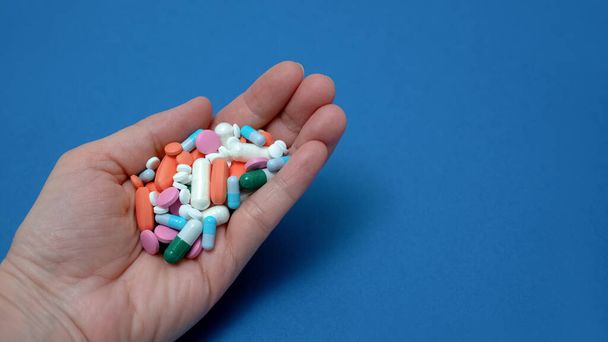 Eine Vielzahl von Medikamenten und Kapseln in der Handfläche einer Frau auf blauem Hintergrund. Das Konzept des Konsums einer großen Anzahl von Drogen - Foto, Bild