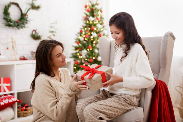 portrait of happy mother giving Christmas gift to her daughter in decorated living room with Christmas tree - Foto, Bild