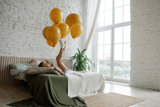 Girl with yellow balloons having fun on the bed in the bedroom. - Foto, imagen