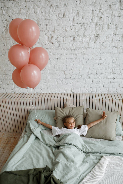 Girl with pink balloons in her hands woke up in bed in the bedroom. - Photo, Image