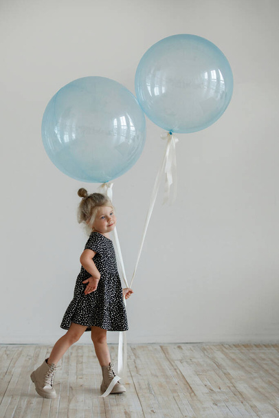 Little girl with a blue balloon in a dress posing in the studio. - Фото, зображення