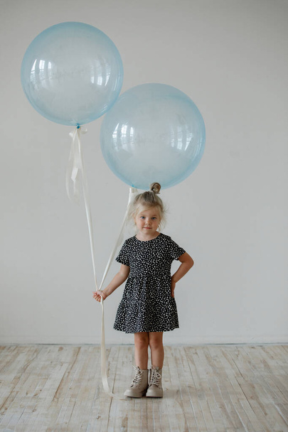 Egy kislány egy kék lufival egy ruhában, pózol a stúdióban.. - Fotó, kép