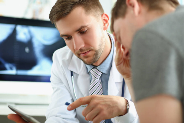 Een jonge arts toont de gezondheidsinformatie aan de man op de tablet - Foto, afbeelding