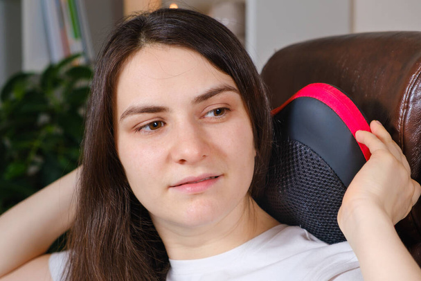 Una donna si siede su una sedia con un cuscino da massaggio e fa un massaggio al collo. - Foto, immagini