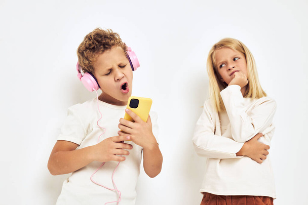 Two preschool children boy and girl headphones with phone entertainment light background - Foto, imagen