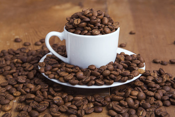 コーヒーカップ付きの素朴な木の表面に新鮮な焙煎コーヒー豆が注がれています. - 写真・画像
