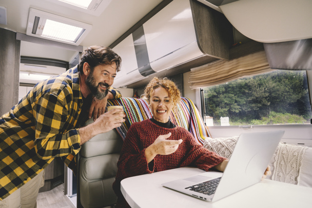 Adult couple enjoy work together using laptop computer sitting inside camper vehicle. - 写真・画像