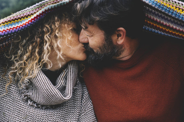 Couple in love kissing under a colorful woolen blanket. Concept of mature people in relationship and life forever. - 写真・画像