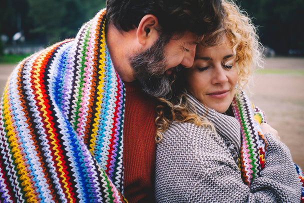 Romantisches erwachsenes Paar bleibt mit Gefühl und Liebe unter einer bunten Wolldecke im Outdoor-Park zusammen. - Foto, Bild