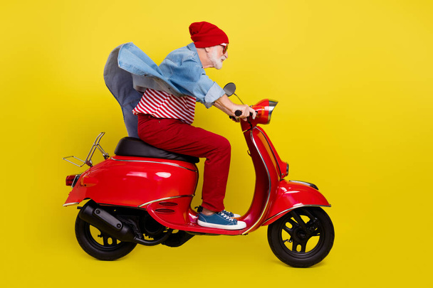 Profile side view portrait of elderly retired pensioner man riding moped having fun isolated over bright yellow color background - 写真・画像
