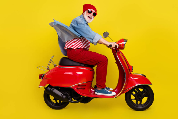Profile side view portrait of elderly retired pensioner cheery man riding moped isolated over bright yellow color background - 写真・画像