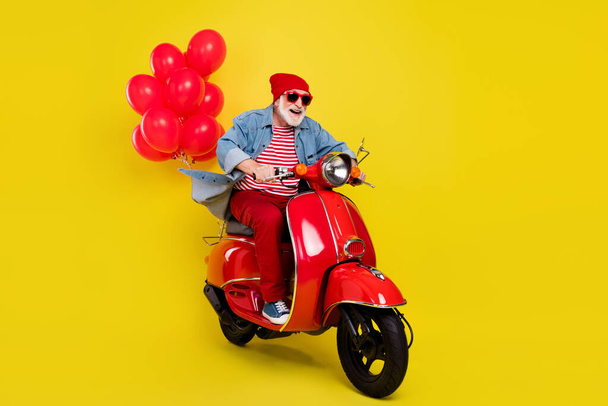 Portrait of elderly retired pensioner cheerful man riding moped having fun isolated over vivid yellow color background - Foto, afbeelding