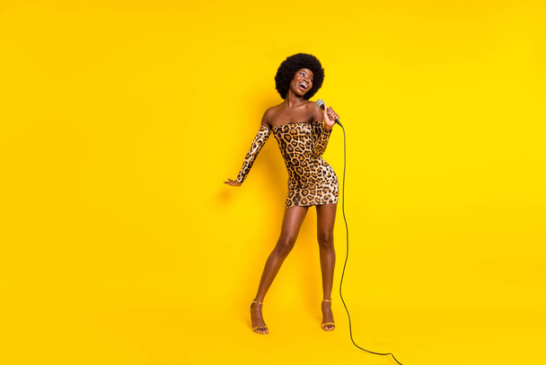 Pleine longueur taille du corps photo fille bouclée portant robe léopard chantant sur scène isolé couleur jaune vif fond - Photo, image