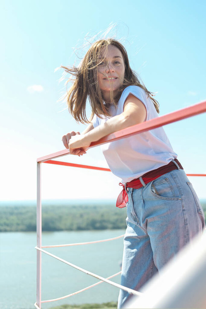 mladá žena stojící nad nábřežím řeky na balkóně nebo terase s výhledem na krajinu. vítr ženské vlasy. relaxovat a zůstat v klidu, můj čas - Fotografie, Obrázek