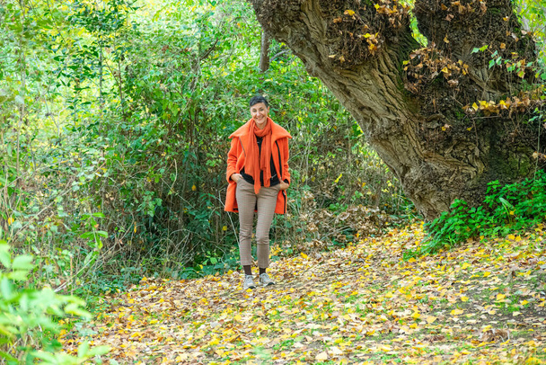 μια μεσήλικη γυναίκα με πορτοκαλί παλτό που ποζάρει στο πάρκο - Φωτογραφία, εικόνα