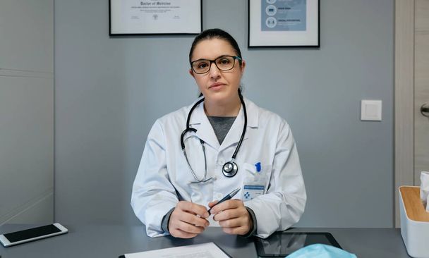 Γυναίκα γιατρός κοιτάζει κάμερα στο γραφείο της - Φωτογραφία, εικόνα
