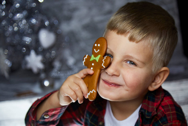 Adorable cheerful toddler hides behind Christmas gingerbread among festive decorations. Atmospheric, aesthetic home for New Years Eve. Good mood. Cheerful baby boy. Joyful, warm cozy home concept - Photo, Image