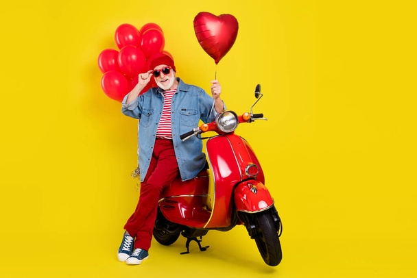 Portrait of elderly retired pensioner trendy cheery man sitting on moped hold heart isolated over vivid yellow color background - 写真・画像