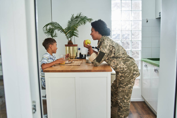 Woman in military uniform chatting with pleasure with her little son during the breakfast - Fotoğraf, Görsel