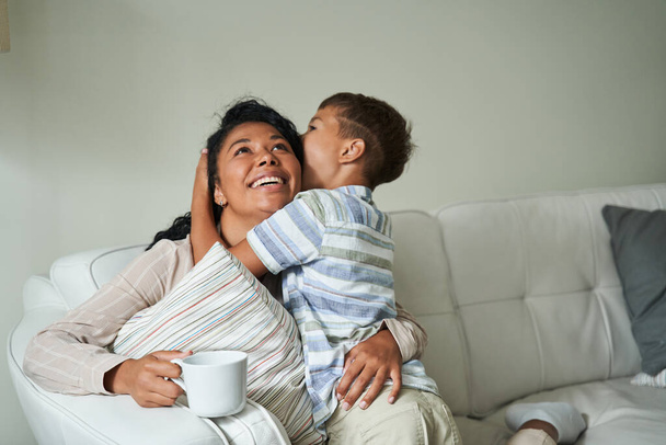 Black boy hugging his happy mother on couch - Fotografie, Obrázek