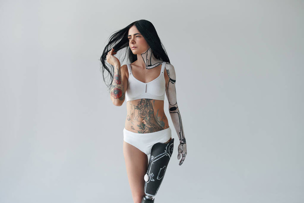 Full length view of the tattooed woman with artificial leg and cyber body art posing at the studio. Unusual appearance concept. Stock photo - Foto, Bild
