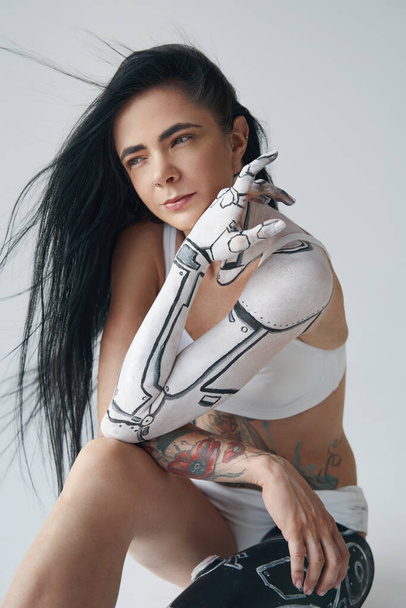 Vertical view of the tattooed woman with cyborg body art and with artificial leg sitting isolated at the studio - Foto, afbeelding