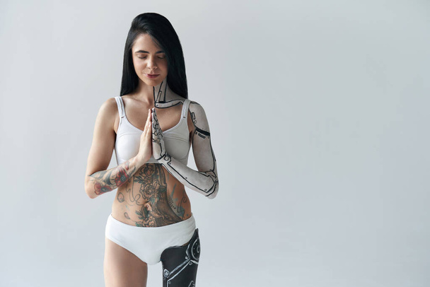 Brunette tattooed girl with cyborg body art and artificial leg meditating calmly - 写真・画像