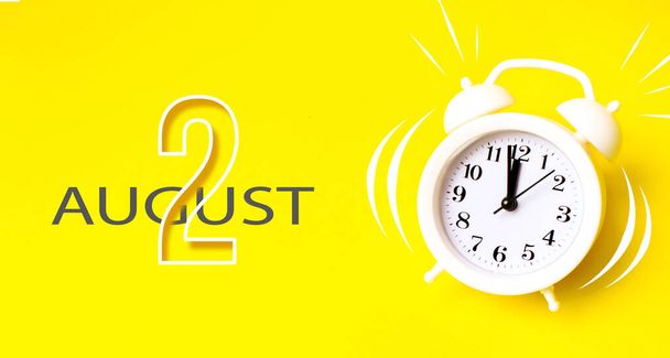 Il 2 agosto. Giorno 2 del mese, data del calendario. Sveglia bianca con giorno di calendario su sfondo giallo. Concetto minimalista di tempo, scadenza, orario di lavoro, mattina. Mese estivo, giorno dell'anno concetto - Foto, immagini