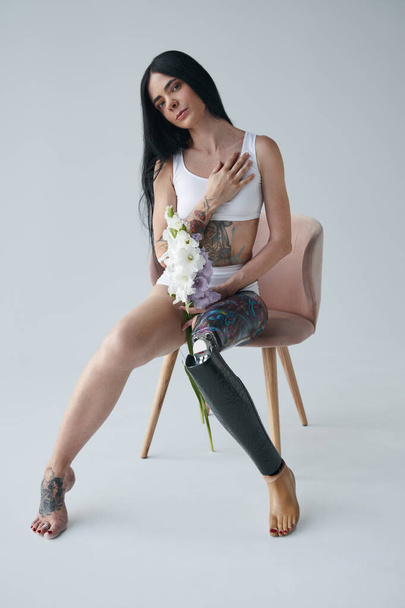 Woman with artificial leg and tattoos at her body holding flowers and smiling - Foto, afbeelding